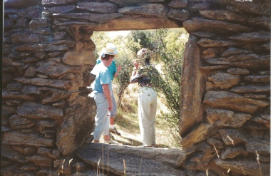Two people standing in a stone doorway of a ruin, looking out towards greenery.