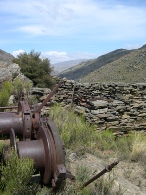 Rusted mining machinery in the foreground with a dry stone wall and hills behind.
