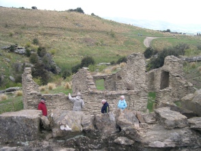 A group of people exploring stone ruins on a hillside with a track winding up behind.