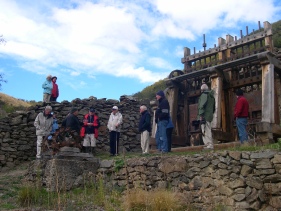 A group of people beside stone walls and old mining machinery, with a wooden stamper battery in the background.