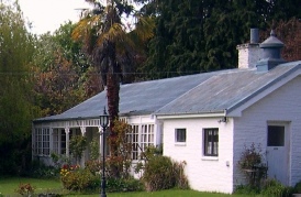 A white weatherboard cottage with a veranda and a palm tree in its garden