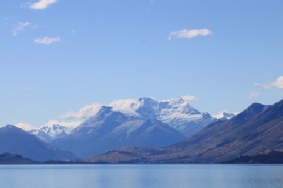 Mountains of the Remarkables range rising above a lake under a partly cloudy sky.