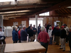 A group of people gathered inside a wooden-beamed hall or woolshed.