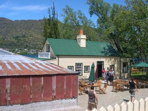 A green-roofed heritage building beside a red corrugated-iron shed, with outdoor tables and people gathered in the courtyard