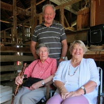 Two women seated and a man standing behind them, posing together inside a rustic barn