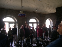 A tour group gathered inside a vaulted stone-arched room, one person at the front gesturing while addressing the group