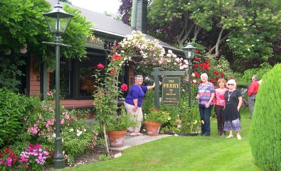 A garden entrance with a sign reading 'The Ferry' among climbing roses, with several people standing beside it