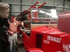 Two people look at a vintage red 1926 Renault fire engine on display inside a museum