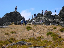 A group of people climbing among large rounded rock tors on an open tussock ridge under a blue sky