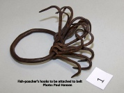 A coiled leather strap fitted with metal fish-poacher's hooks, laid on a table beside a small numbered card, captioned in the photo as a gift from Paul Hansen.
