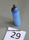 A small blue cylindrical hair-curling powder compact with a metal screw cap, standing on a table beside a card numbered 29.