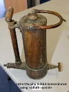 An old copper cylindrical electrolytic rabbit-exterminator device that used sulphuric acid, with a numbered card beside it.