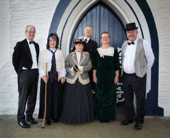 Six people in Victorian-era costume standing together in front of the Arrowtown Gaol's arched stone doorway.