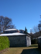 Exterior of the stone Arrowtown Gaol building under a blue sky with snow-dusted hills behind