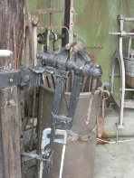A close-up of an old black metal mechanical device among the stored collection of antique items.