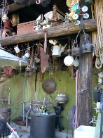 A crowded display of small collectible objects, including bottles, tools and jugs, hanging and stacked under a lean-to shelter.