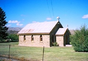 A small stone former Presbyterian church with a corrugated-iron roof and a bell cupola, set against hills.