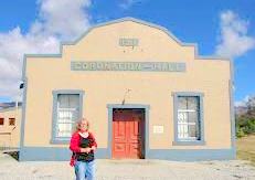 The yellow and blue Coronation Hall building with its name over red double doors, and a woman standing at the entrance.