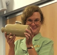 A woman in a green cardigan holds up a ceramic pig-shaped hot water bottle