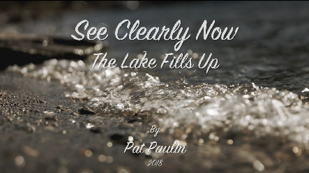 Title card of the short film See Clearly Now: The Lake Fills Up by Pat Paulin, 2018, over a close view of water washing over a stony shore