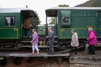 Members standing on a low timber platform between two dark green Kingston Flyer carriages