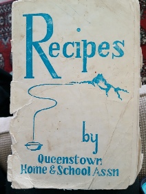 The worn cover of a booklet lettered Recipes by Queenstown Home and School Assn in blue, with a small line drawing of a mountain and a hanging pot