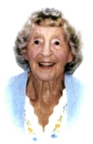 A smiling elderly woman with short white hair in a pale blue jacket over a white top with a floral trim, against a plain white background