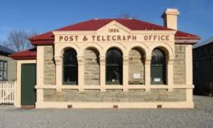 A single storey stone post office with a red roof, three arched openings across the front and the words Post & Telegraph Office cut into the facade
