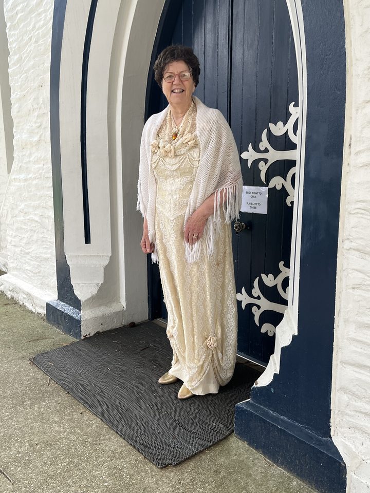 Catherine Brown as Mary ‘Mammy’ Johnston, in a cream lace gown and fringed shawl, standing at a blue arched door with white ironwork