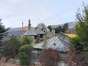 'Whakatipua', Arrow Junction: the roofs and conical turret of the house from across the trees, hills behind