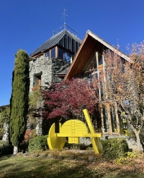 'Whakatipua', Arrow Junction: the stone and timber gable end in autumn, with a large yellow sculpture on the lawn